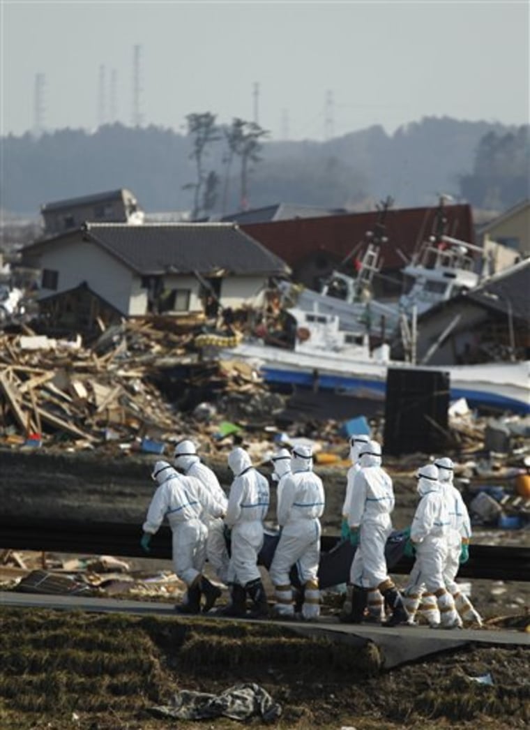 Japanese police officers on Friday carry a body recovered from an area devastated by the March 11 earthquake and tsunami in Namie, Fukushima prefecture, northeastern Japan. In the background is part of the damaged Fukushima Dai-ichi nuclear complex.